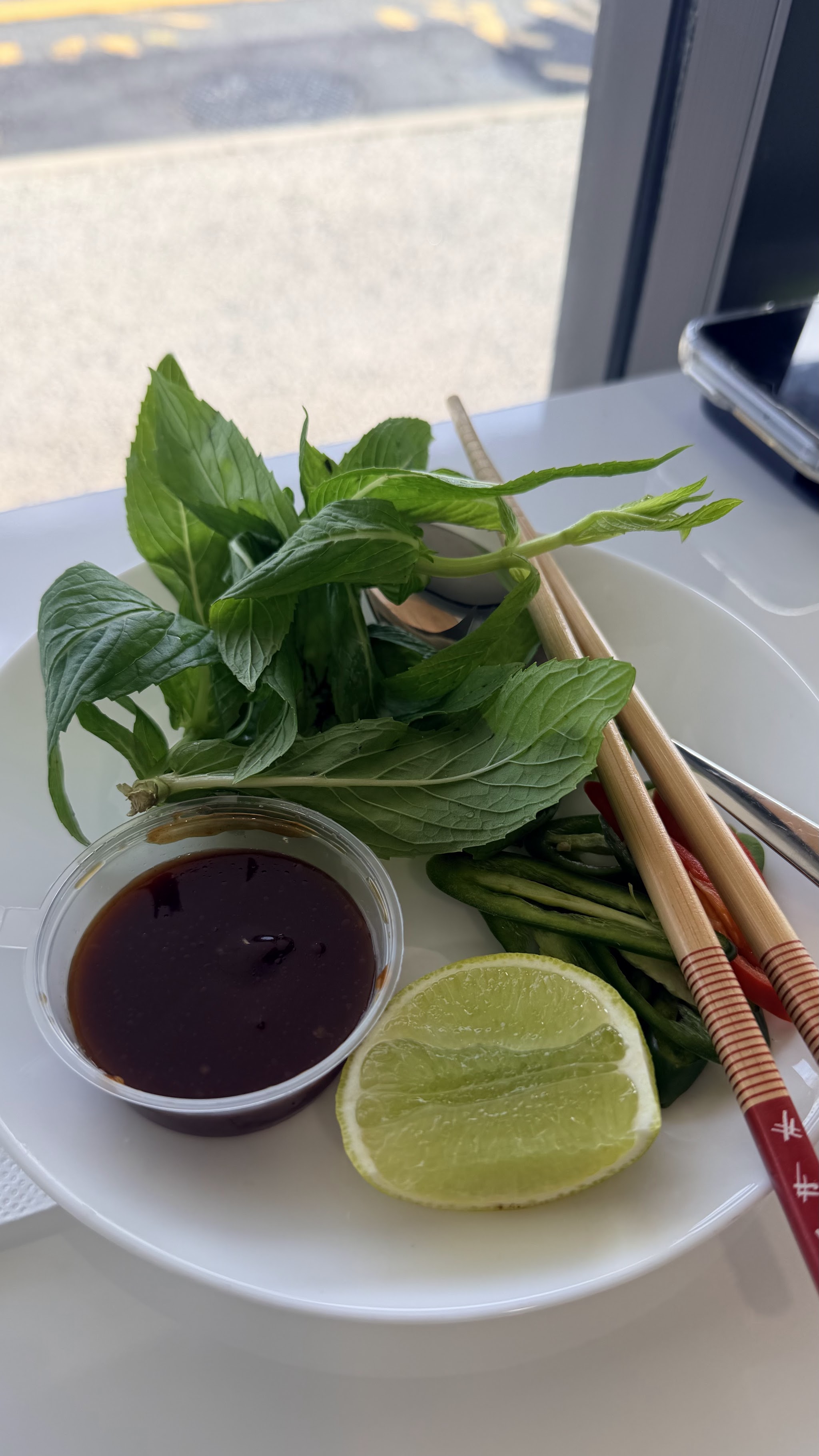 A garnish plate of Vietnamese mint and basil with a lime wedge, dipping sauce and chopsticks