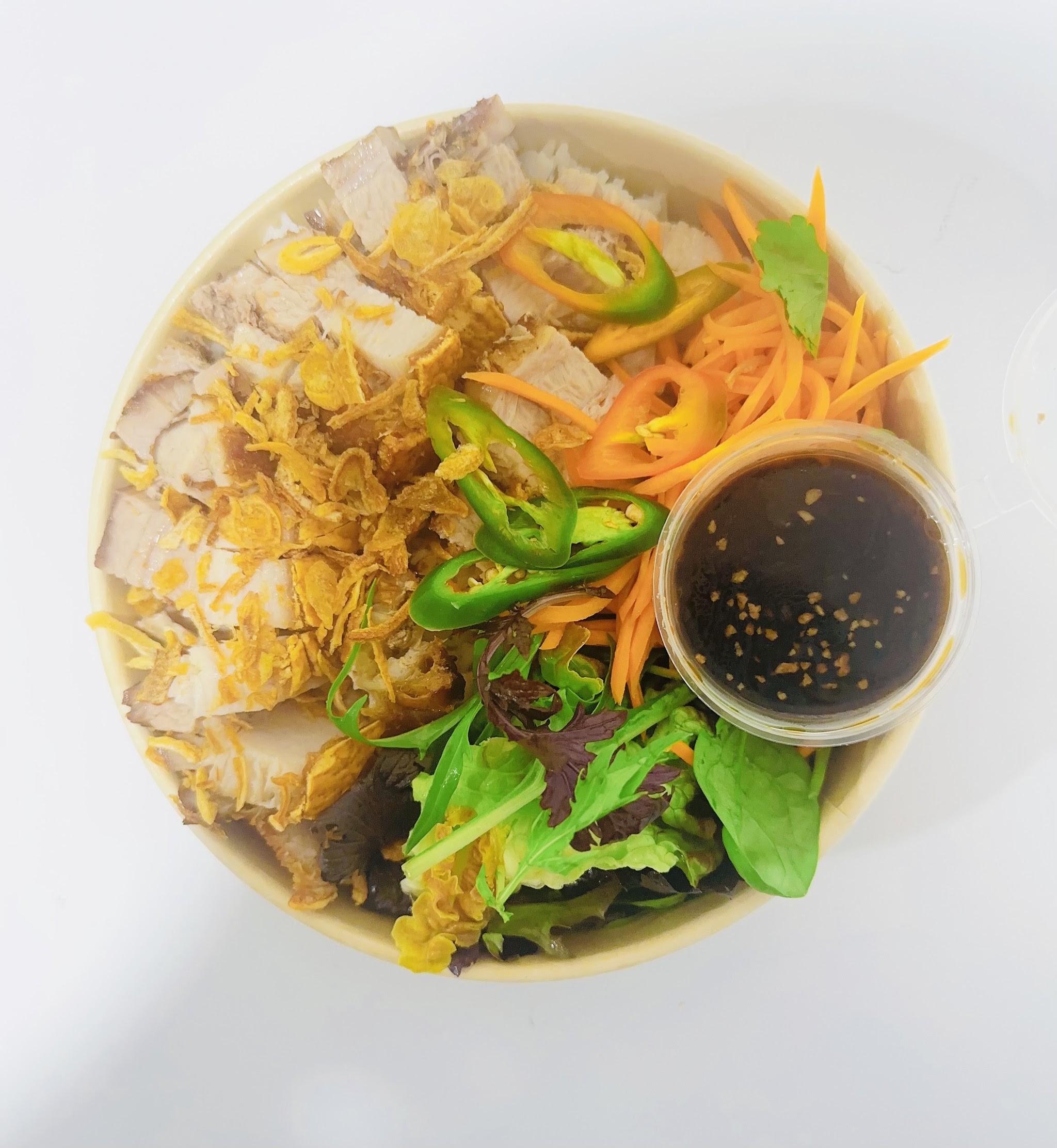 A rice bowl topped with roast pork, crispy shallots, fresh herbs, chilli and pickled carrot