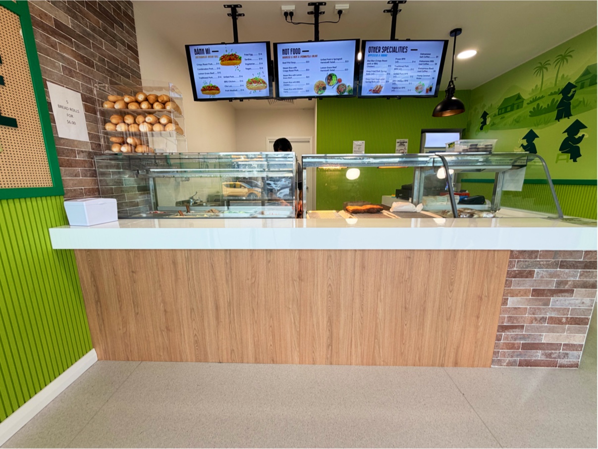 The counter, with fresh baguettes stacked on the bread rack and the menu screens overhead