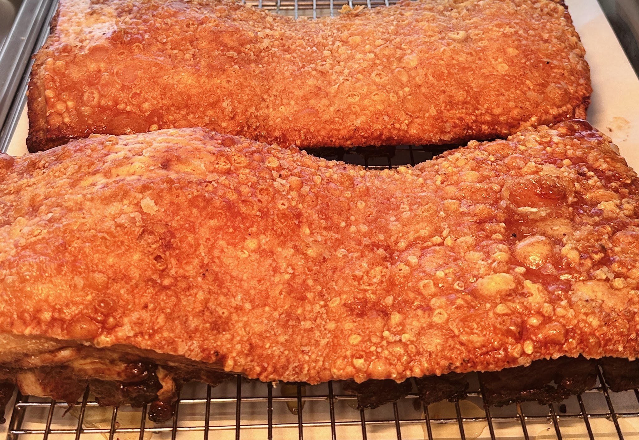 Slabs of crispy roast pork belly with blistered crackling cooling on a wire rack